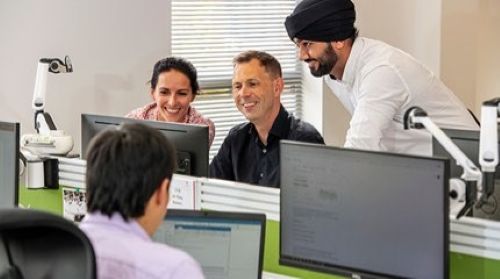 Two people sitting looking at a computer screen and another person standing looking at the screen