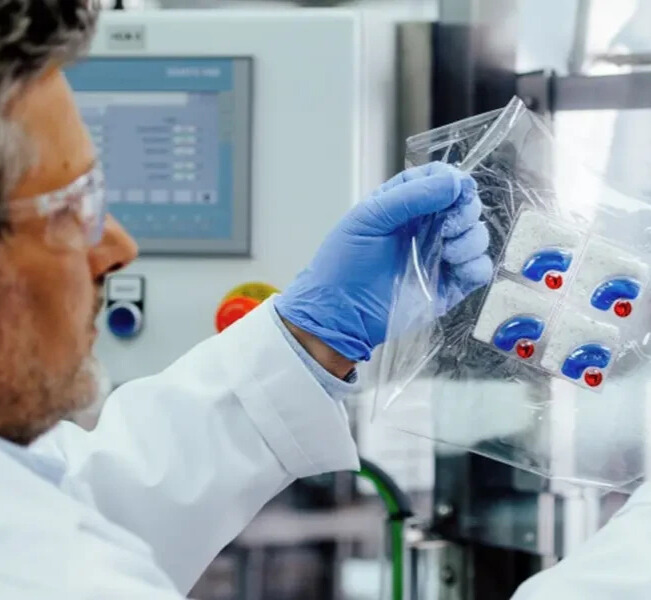 Scientist in gloves inspecting blister-packed capsules inside a sealed bag.