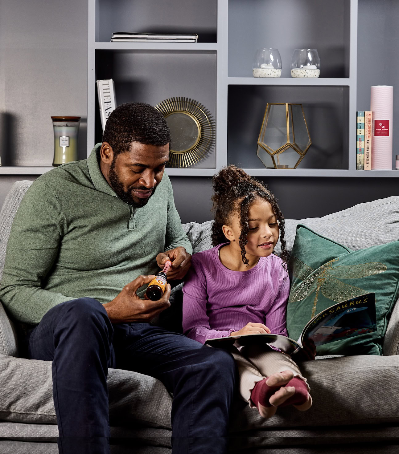 Man and young girl reading together on a couch, holding a medicine bottle.