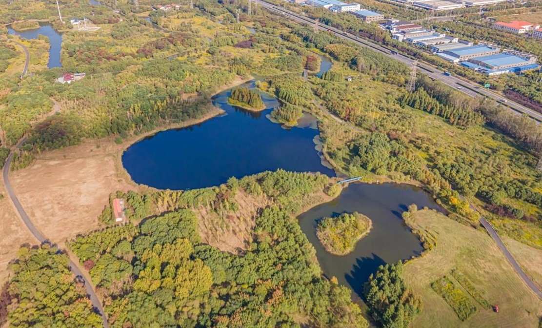 Aerial view of lakes, wetlands, and green landscape with nearby roads and industrial buildings in the distance