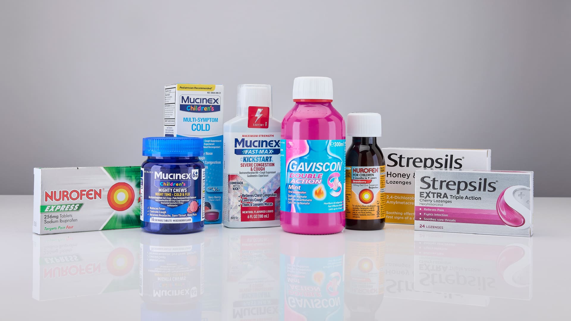 Selection of over-the-counter cold, flu, pain relief, and digestive health products displayed on a white surface