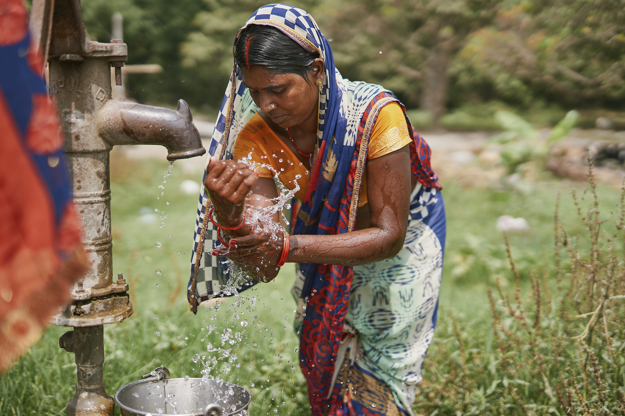 Woman washing her hands at an outdoor water pump