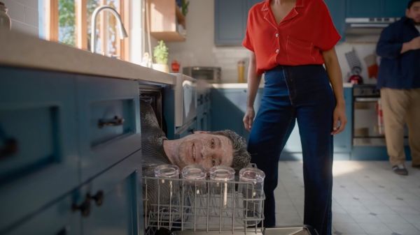 Person peeking out from an open dishwasher in a kitchen while others stand nearby smiling