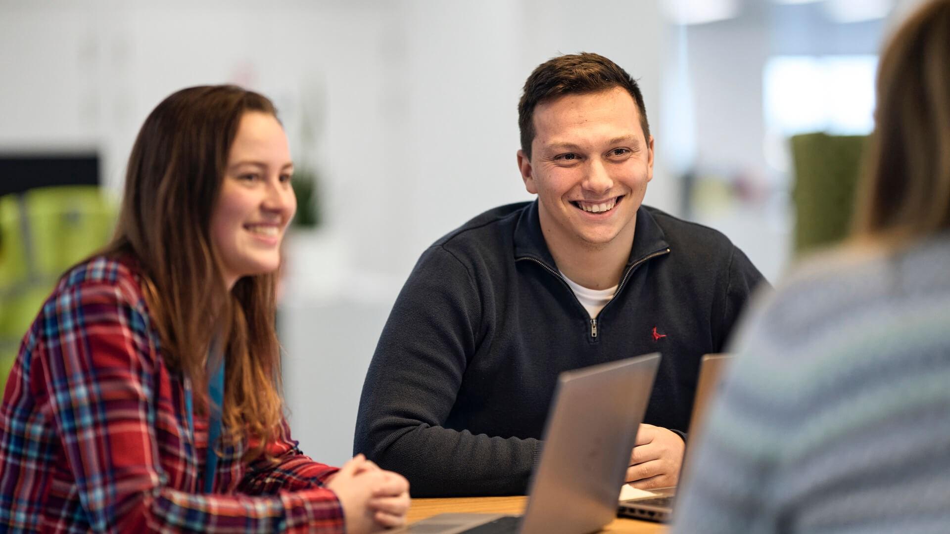 Colleagues smiling and collaborating during a meeting around a table with laptops