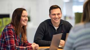 Colleagues smiling and collaborating during a meeting around a table with laptops