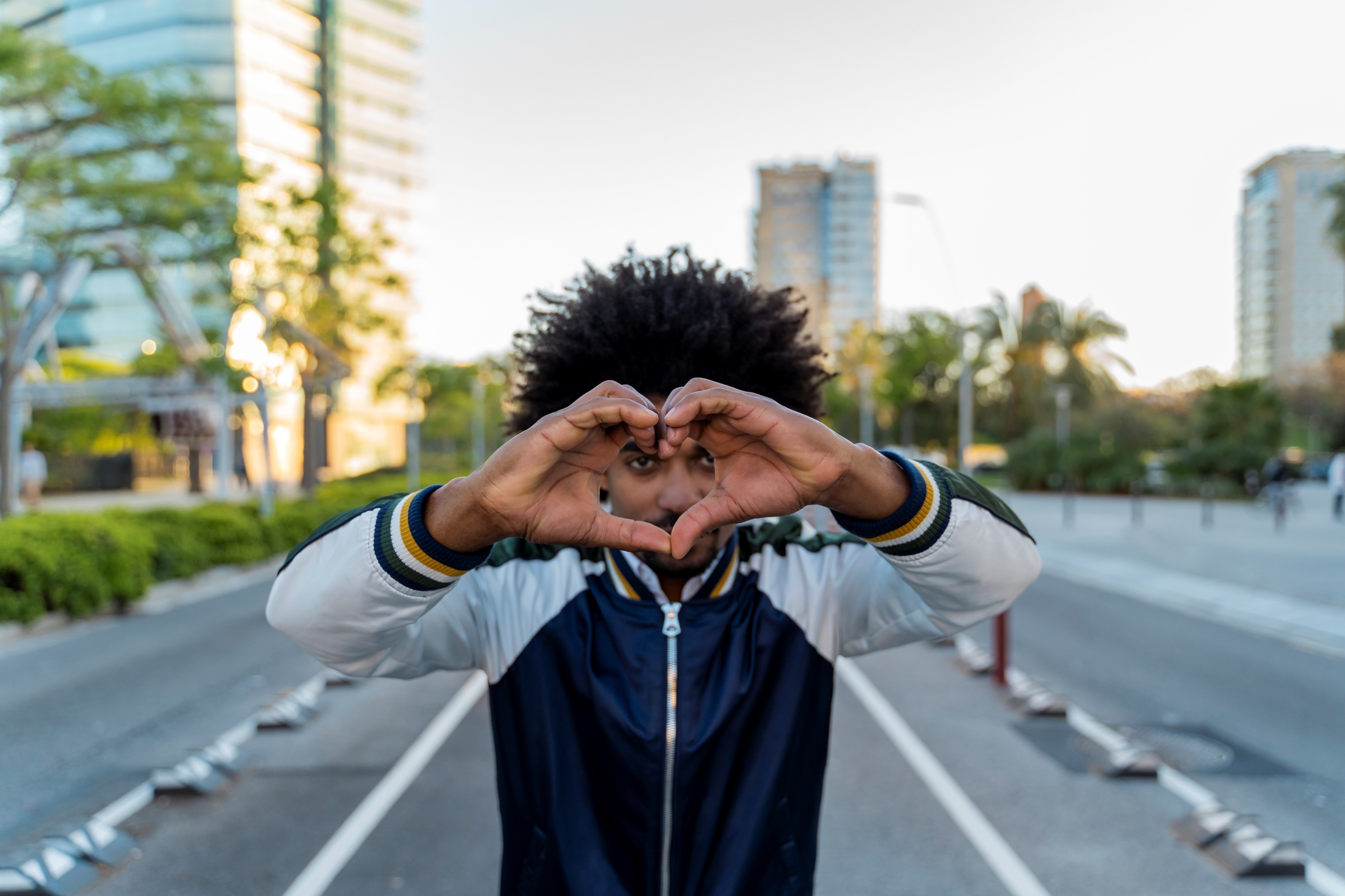 Person making a heart shape with their hands while standing on a city street outdoors