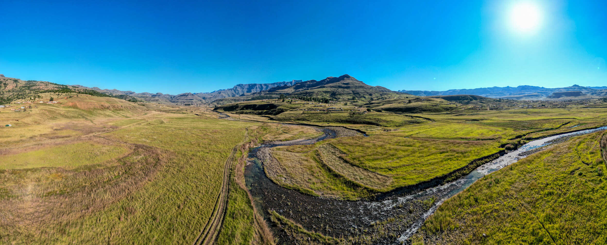 Wide landscape of a grassy valley with a winding river under a clear blue sky