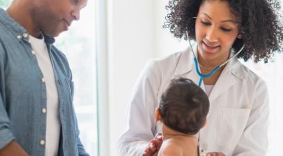 Doctor examining a baby with a parent standing nearby.