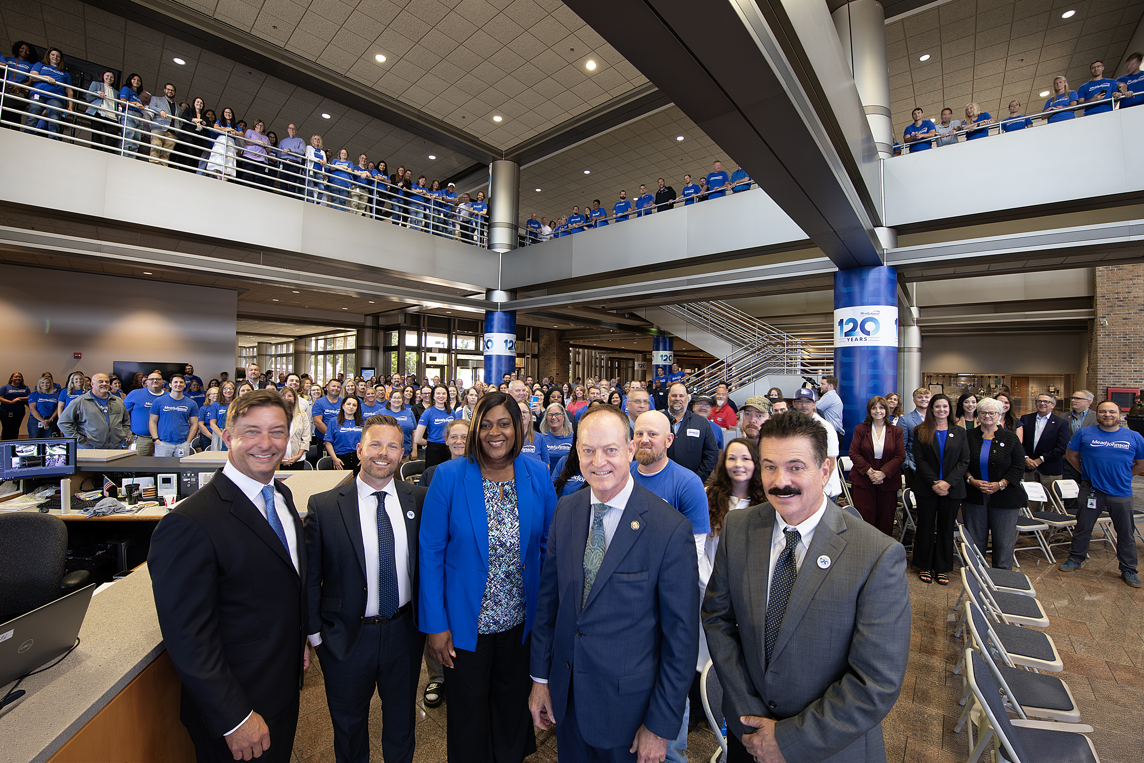 Large group of employees and community leaders gathered for a company event in a corporate atrium setting