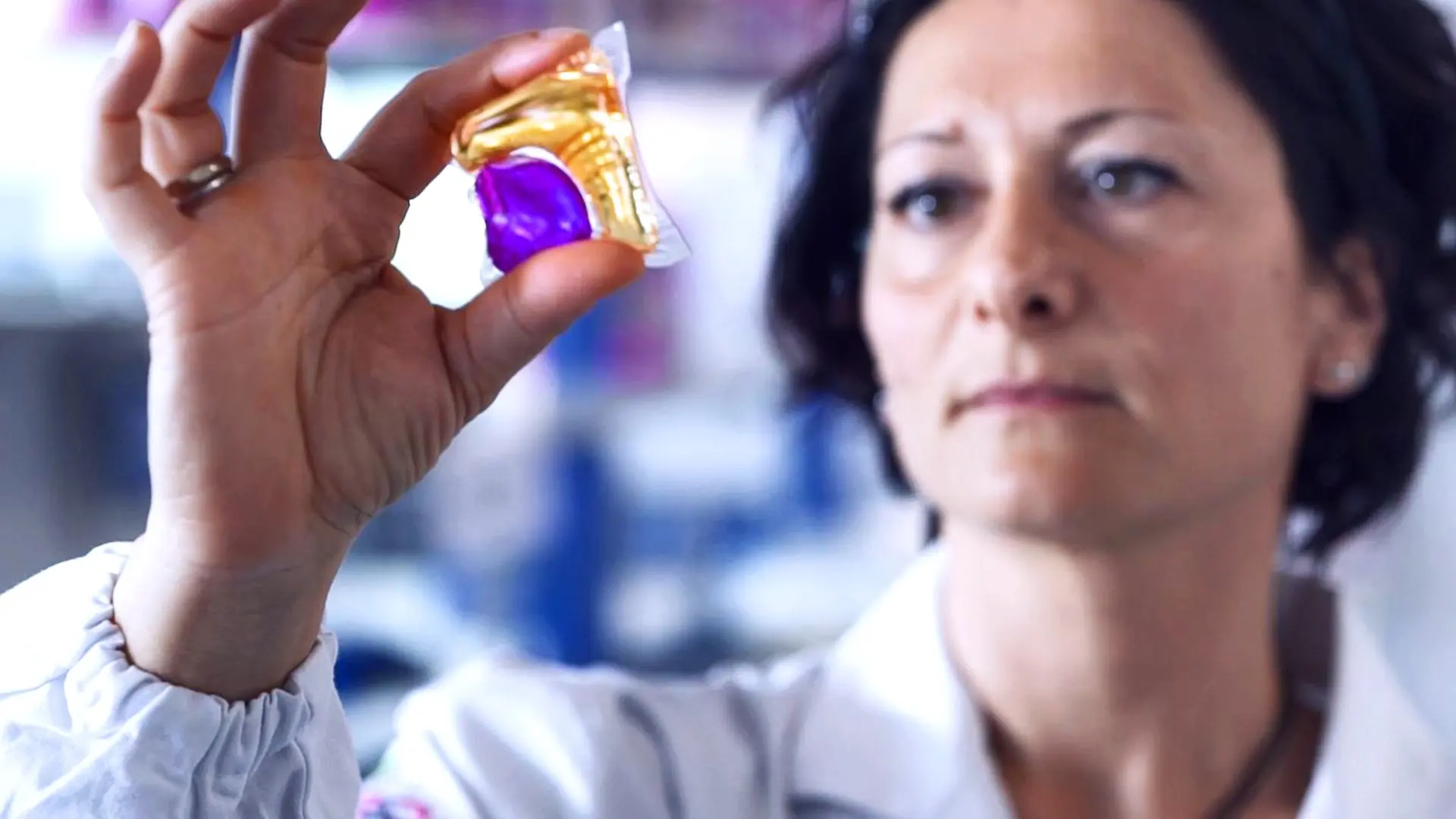 Scientist examining a purple gel capsule in a laboratory setting.