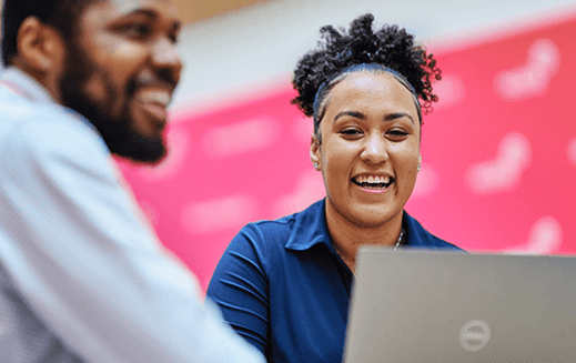 Two colleagues smiling and collaborating while working on a laptop in an office setting