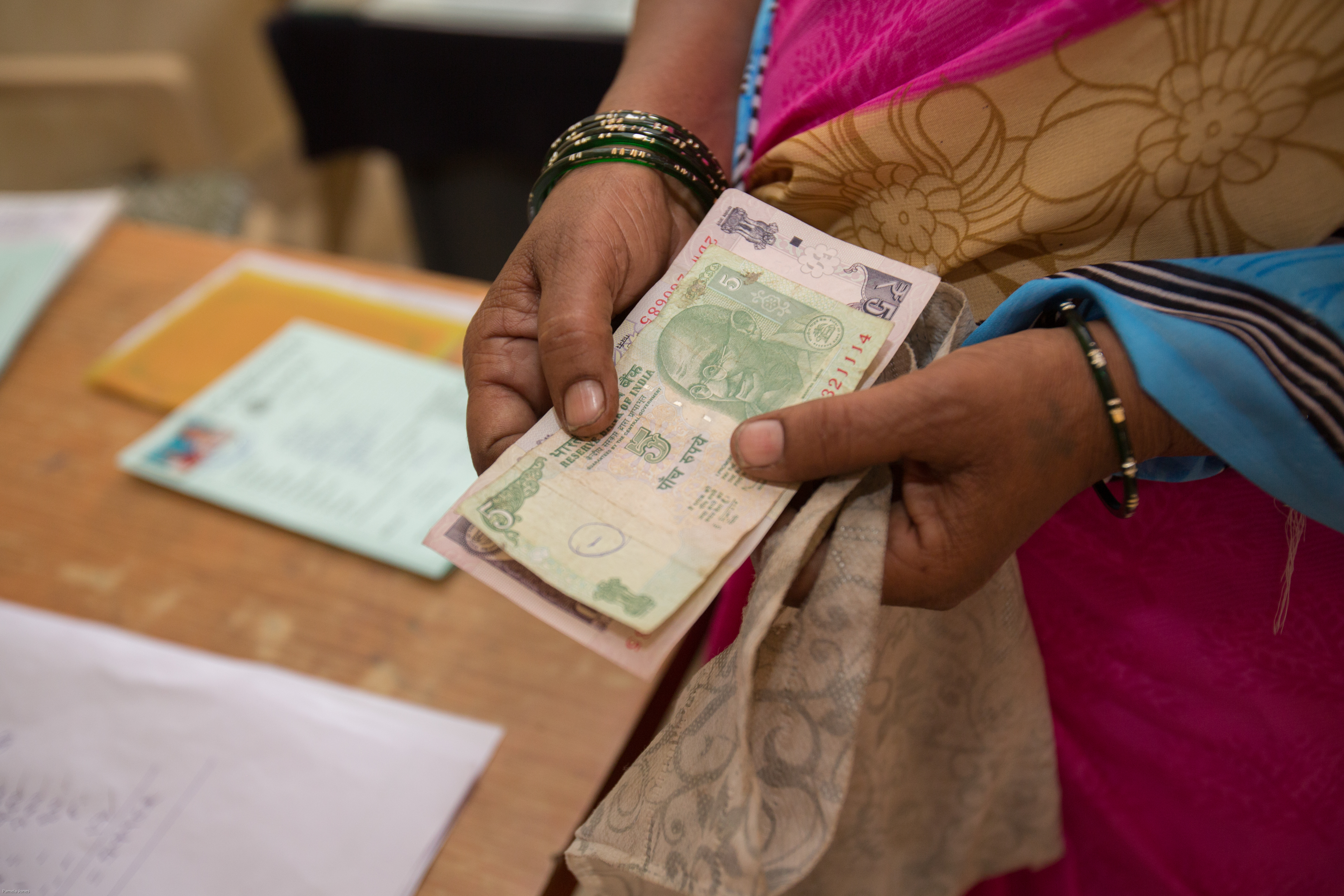 A person wearing traditional clothing and bangles is holding several Indian currency notes in their hands.