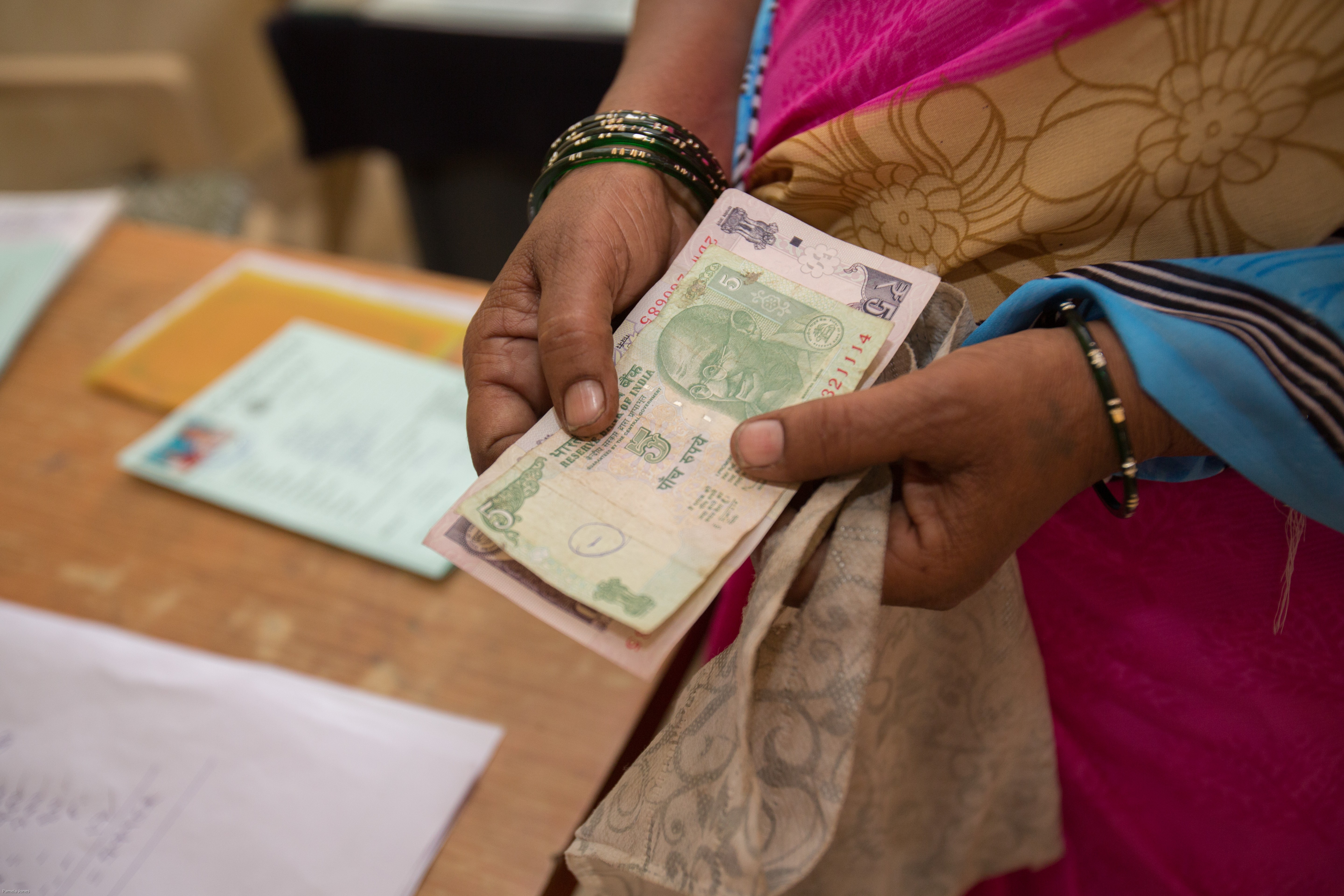 A person wearing traditional clothing and bangles is holding several Indian currency notes in their hands.