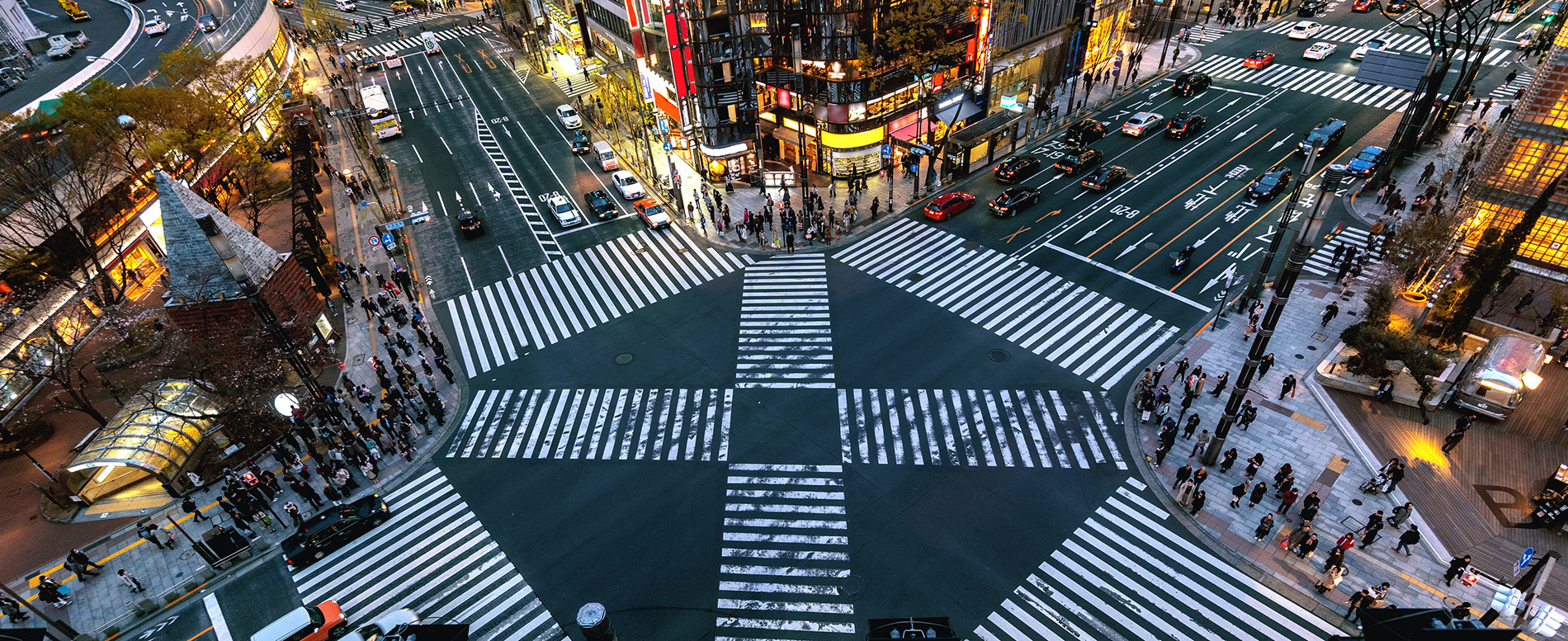 Busy city intersection with multiple crosswalks, vehicles, and pedestrians waiting to cross at dusk