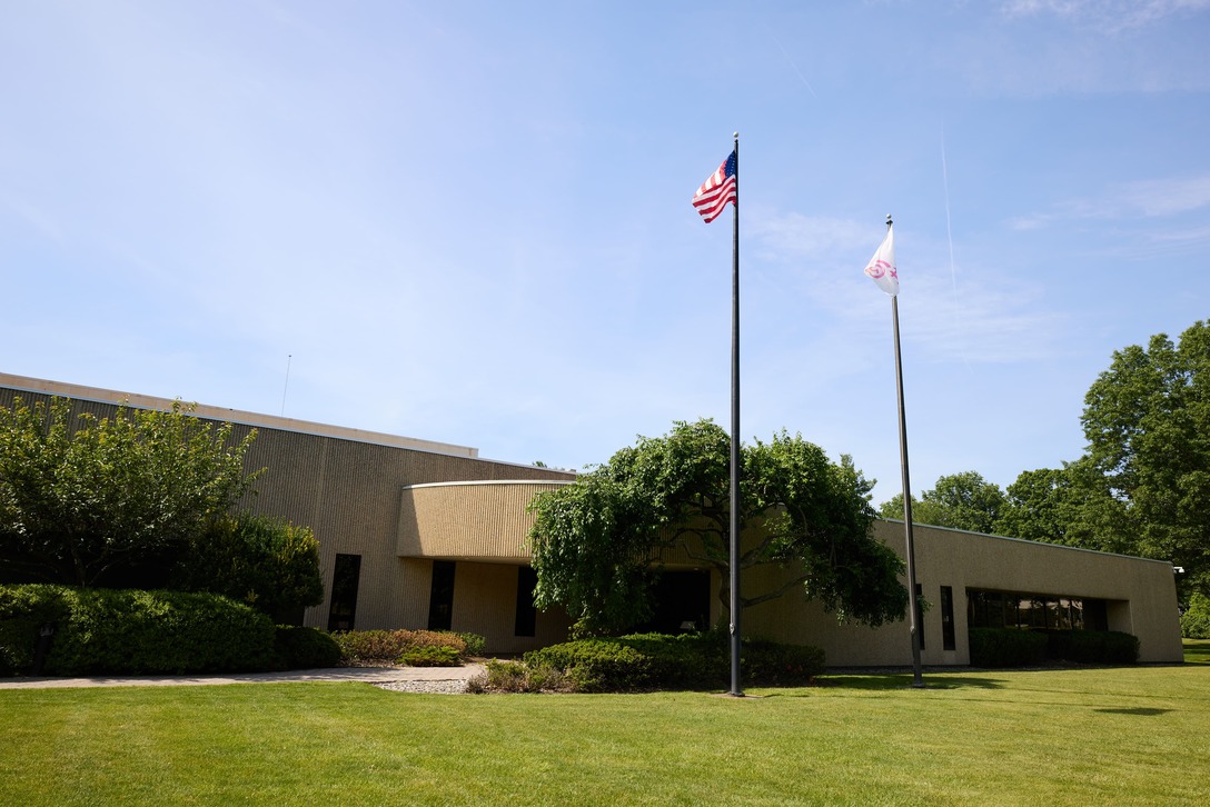 A single-story office building with a textured exterior, surrounded by greenery, with an American flag and another flag flying on tall flagpoles in front
