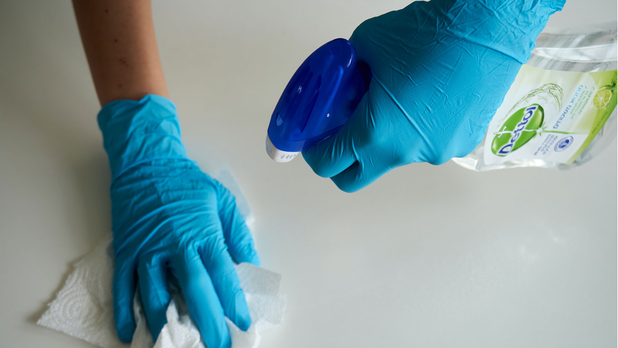 Hands wearing gloves spraying and wiping a countertop with disinfectant