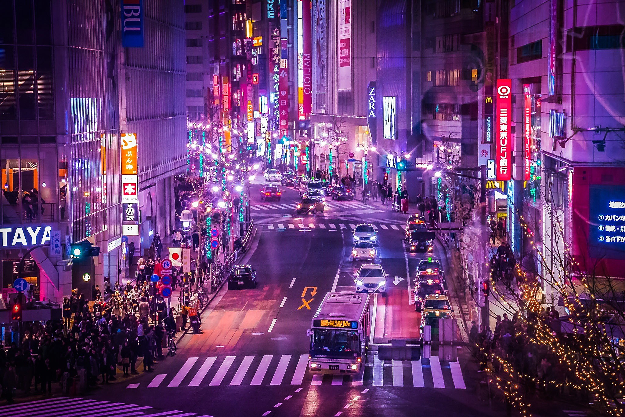 Image of an Asian city road at night-time , the pavements are full of commuters and shoppers