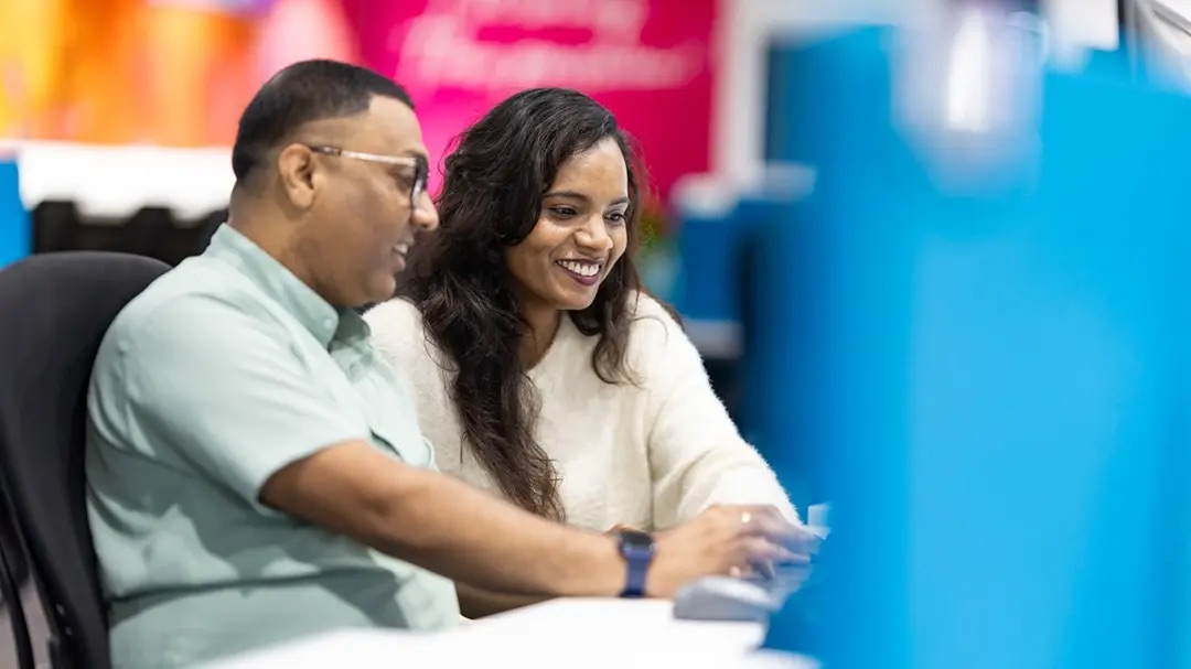 Two coworkers smiling while looking at a laptop screen together.