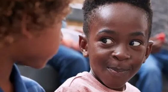 Child smiling and glancing sideways while interacting with another child.