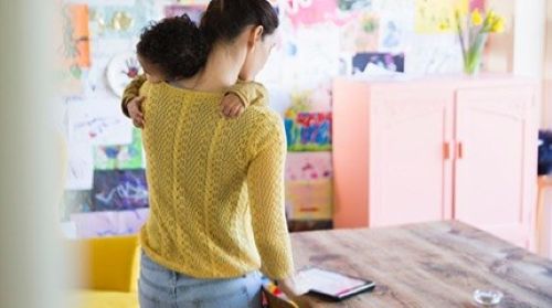 Parent standing up holding a baby looking at an iPad in a nursery