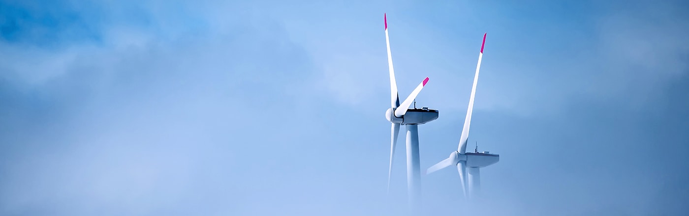 Wind turbines rising above clouds against a blue sky