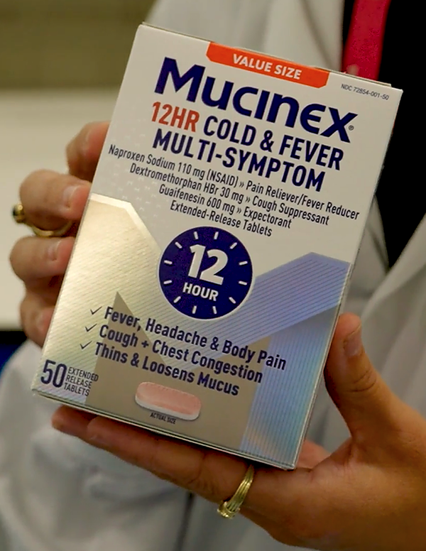 A close-up of a person holding a Mucinex 12-hour cold and fever multi-symptom relief package