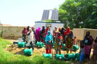 Women and children at a solar-powered water station with green rolling water containers.