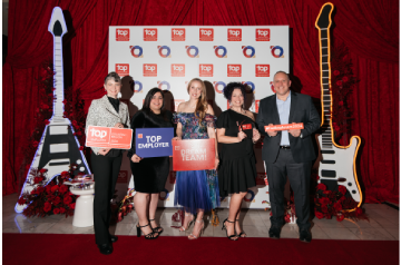 A team celebrating a Top Employer recognition at an awards event, posing with achievement signs in front of a branded backdrop and decorative stage display