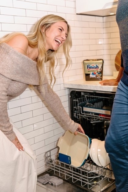 Woman loading dishes into a dishwasher in a kitchen, with Finish Ultimate detergent displayed nearby