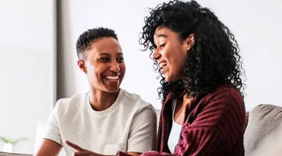 Two women smiling and talking while sitting together.
