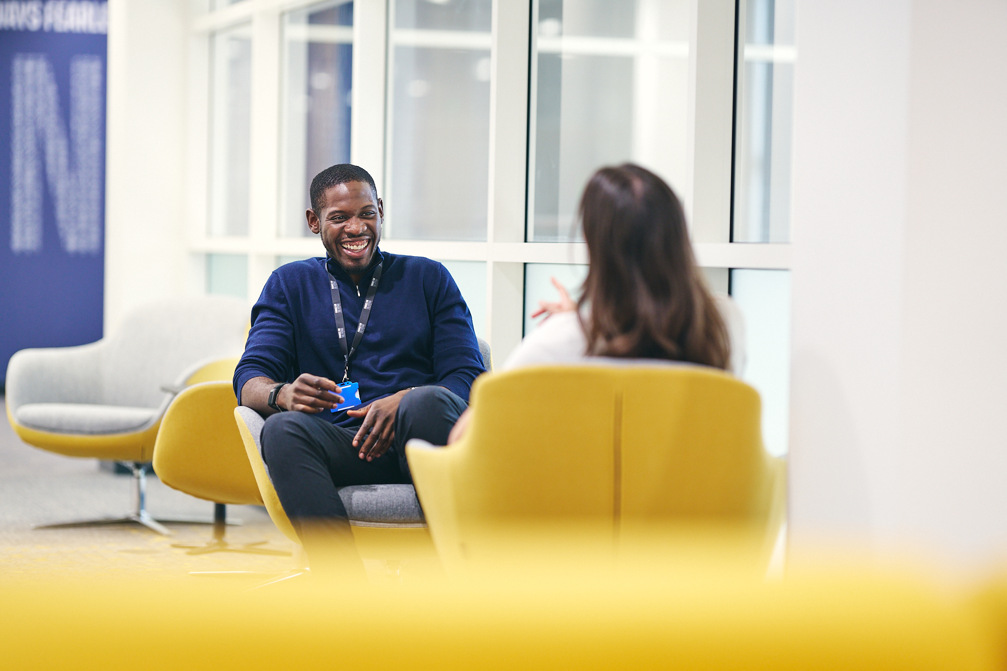 Two colleagues seated in yellow chairs having a friendly conversation in a bright office.