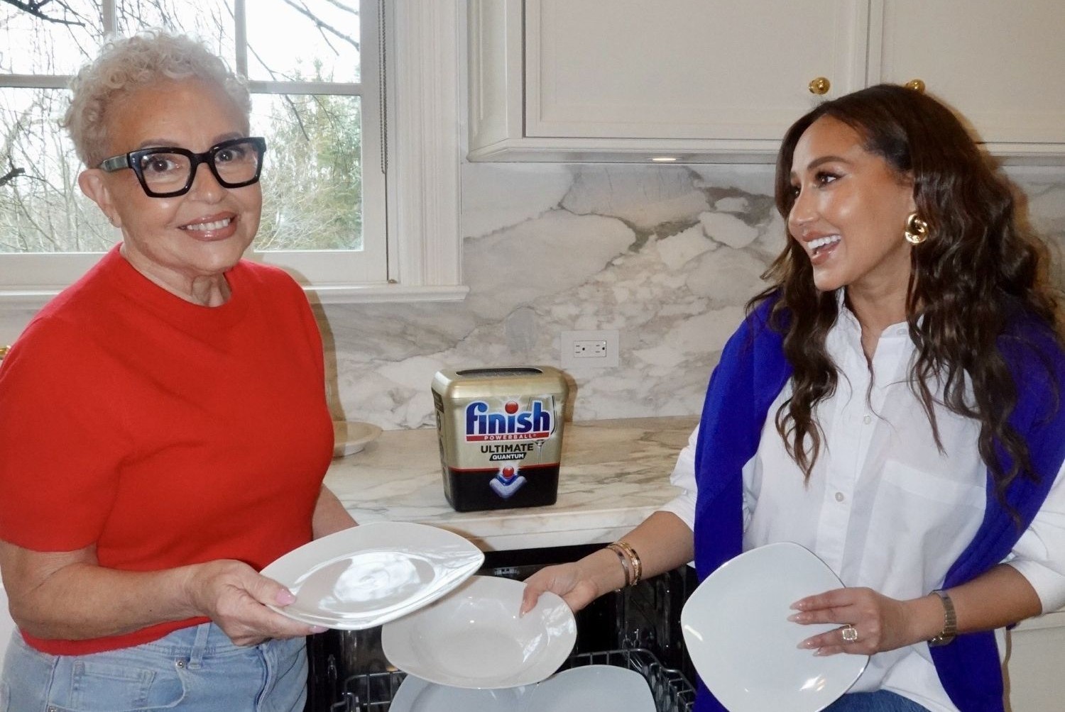 Two women holding dishes and smiling in a kitchen with a Finish product on the countertop