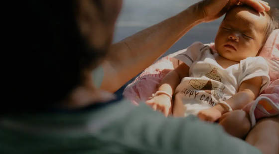 Adult gently touching a sleeping baby’s head while holding them.