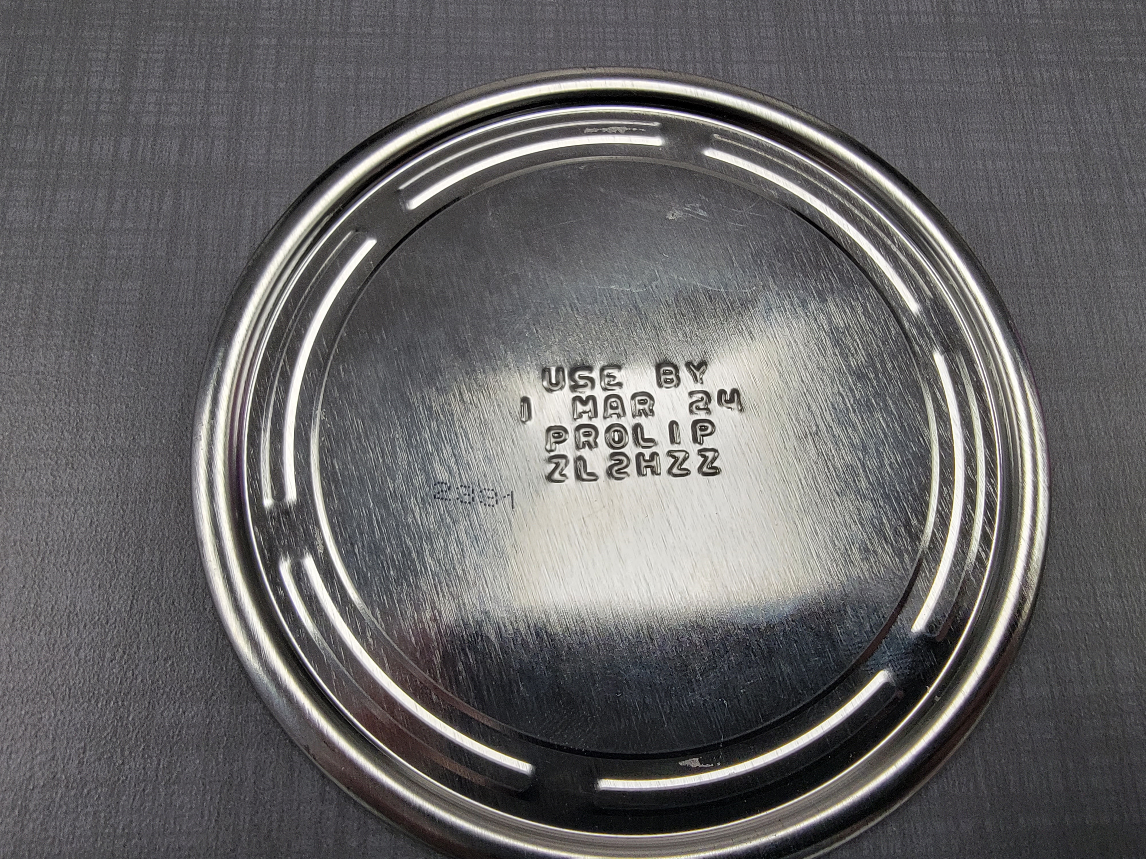 Bottom of infant formula can showing embossed use-by date, lot code, and product identification markings on the metal base