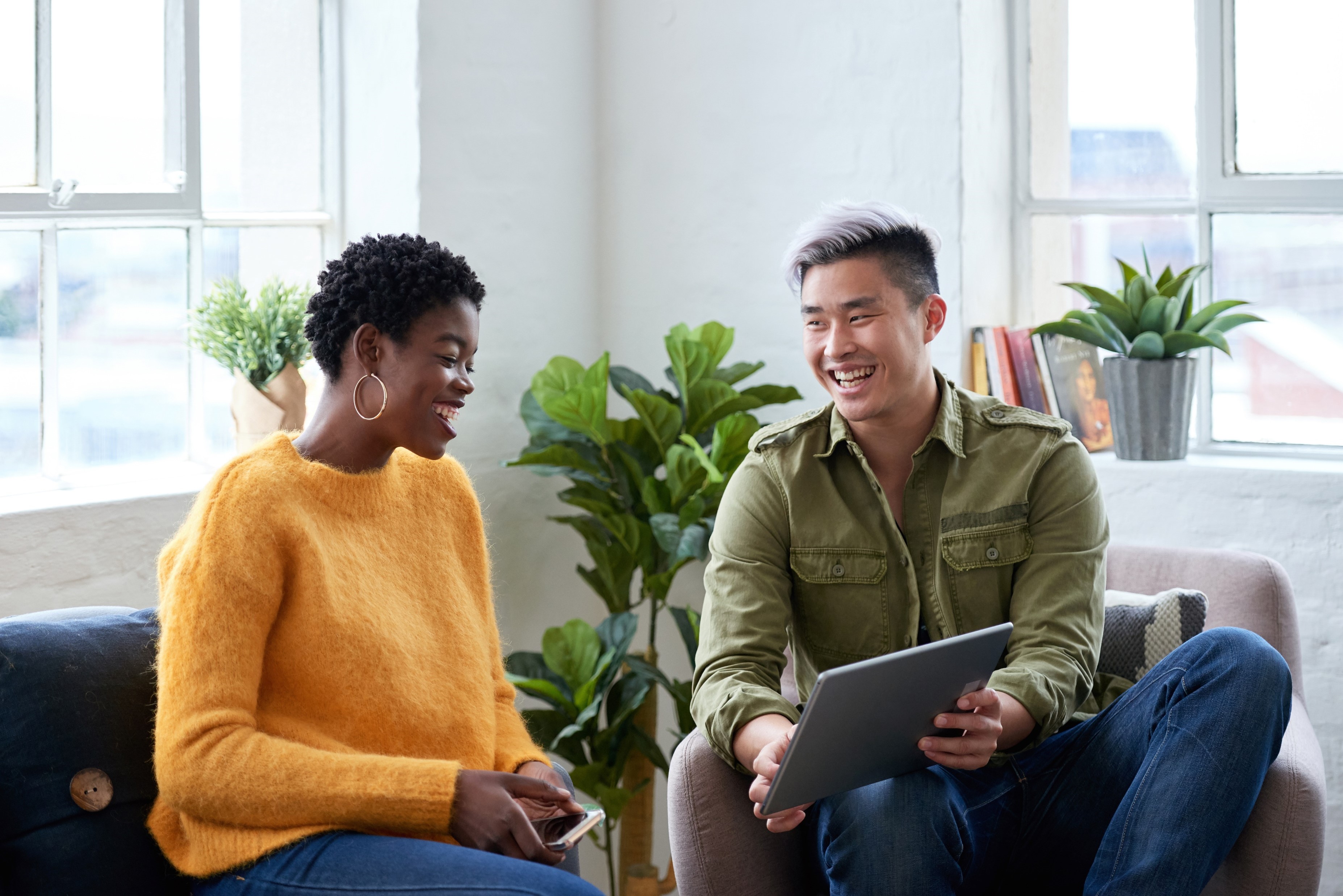 Two colleagues smiling and talking while using a tablet in a bright office space