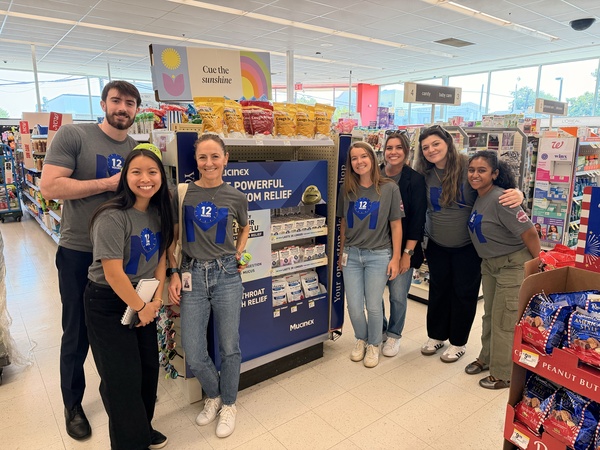 A Mucinex promotional team posing beside a branded cold and flu display in a pharmacy