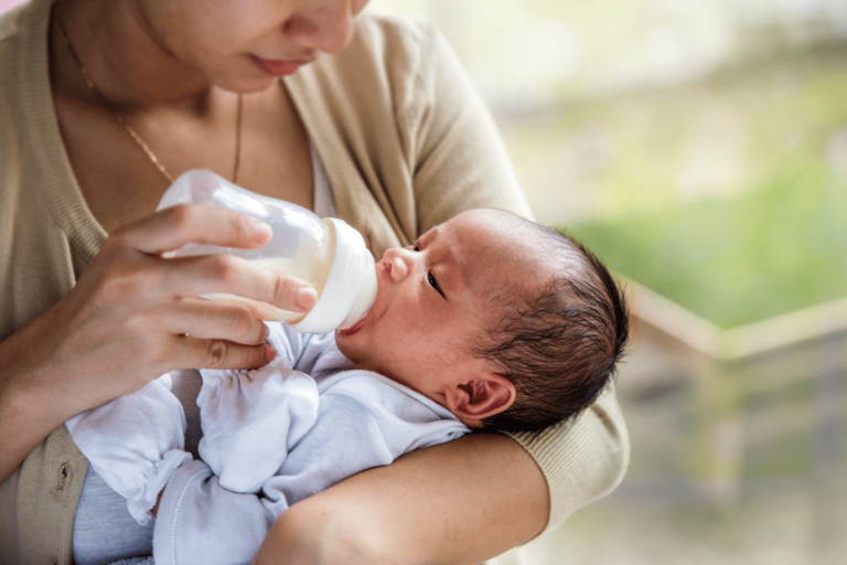 Adult feeding a baby with a bottle while holding them in their arms indoors