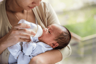 Adult feeding a baby with a bottle while holding them in their arms indoors