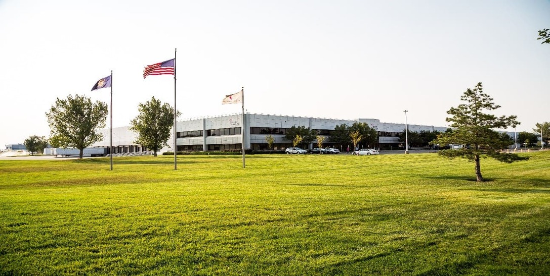 A large modern office complex with landscaped gardens, multiple parking spaces including handicapped spots, and a multi-level parking structure surrounded by greenery