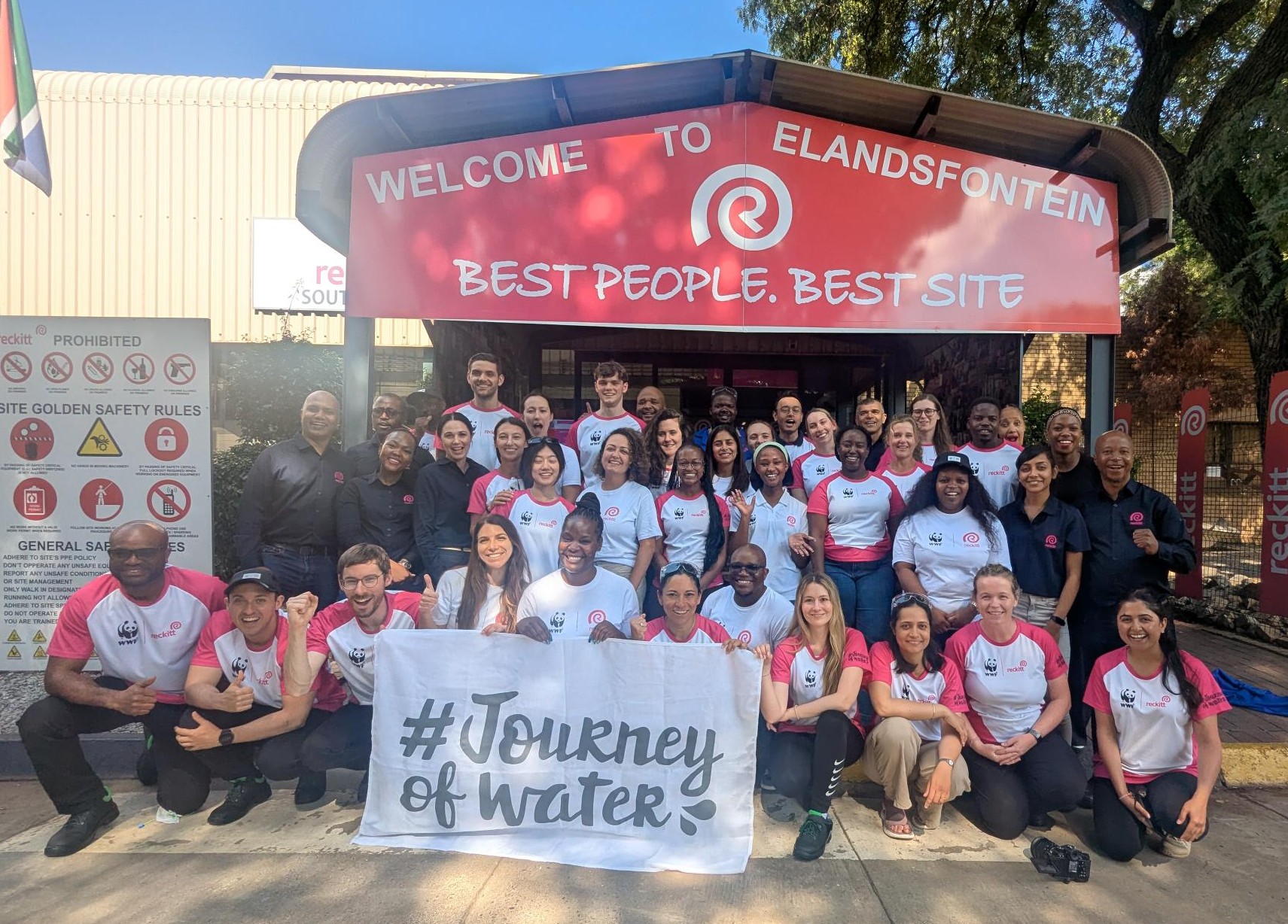 Group of volunteers posing outside a site entrance with a “Journey of Water” banner