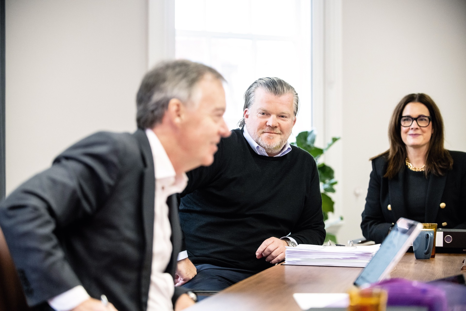 Professionals engaged in a business meeting around a conference table, discussing documents in a bright office setting