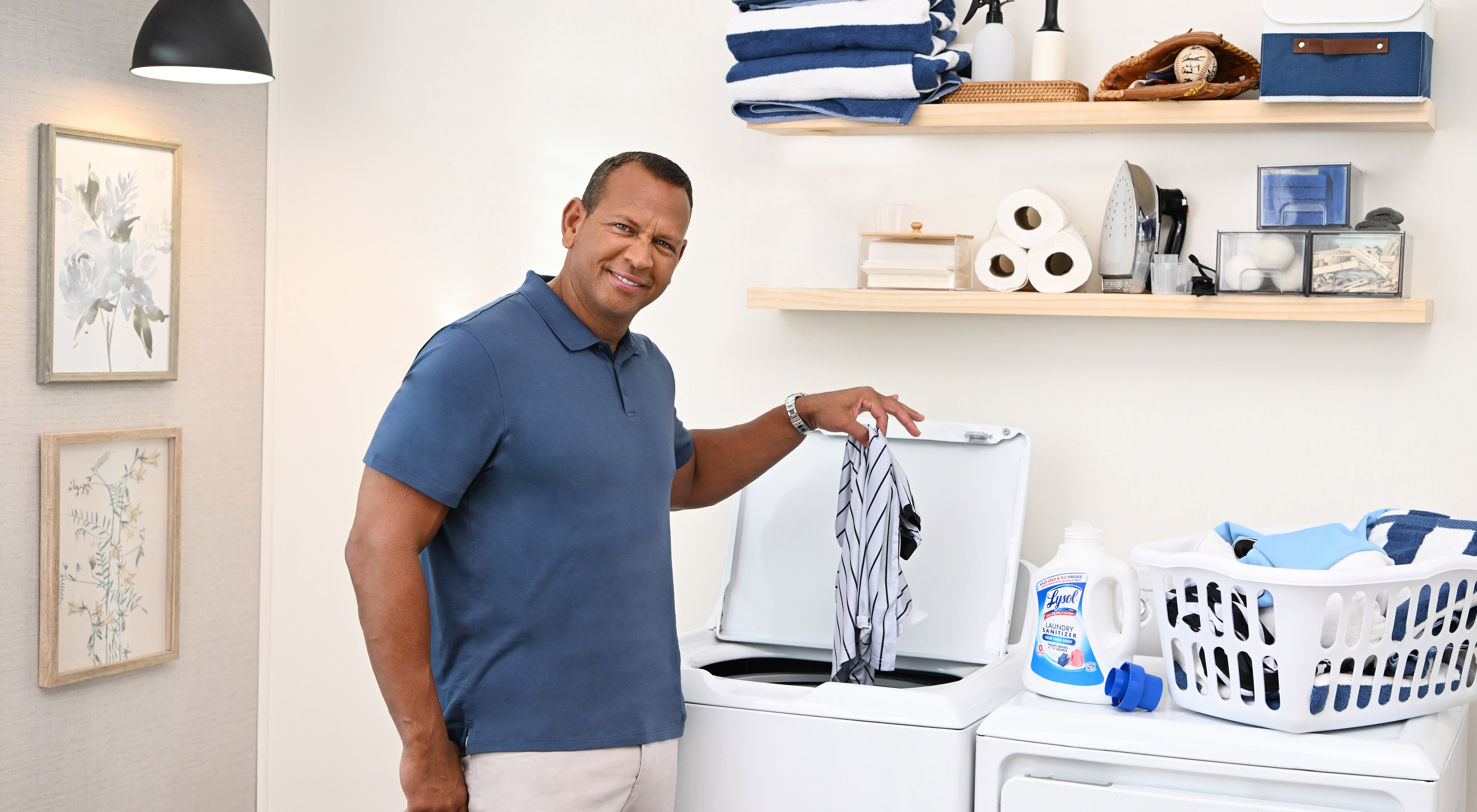 Man loading laundry into a washing machine beside Lysol Laundry Sanitizer and a basket of clothes