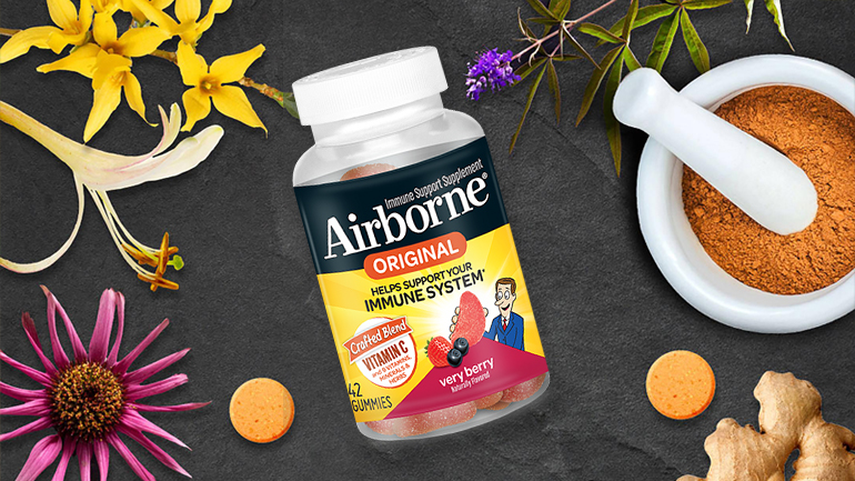 A bottle of Airborne Original immune support gummies in very berry flavor surrounded by flowers, a mortar and pestle with powder, and ginger root