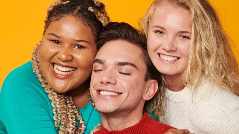 Three people closely posed together against a bright yellow background, expressing warmth and friendliness.