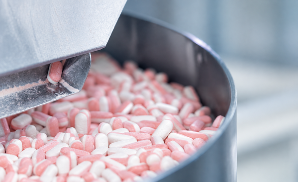 Close-up of pink and white tablets being processed in pharmaceutical manufacturing equipment