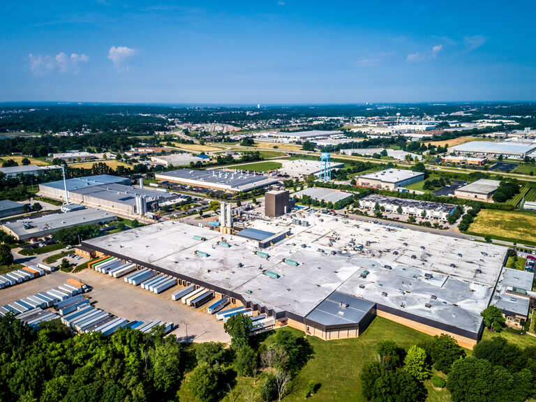 Aerial view of a large industrial manufacturing facility surrounded by warehouses, roads, and green space