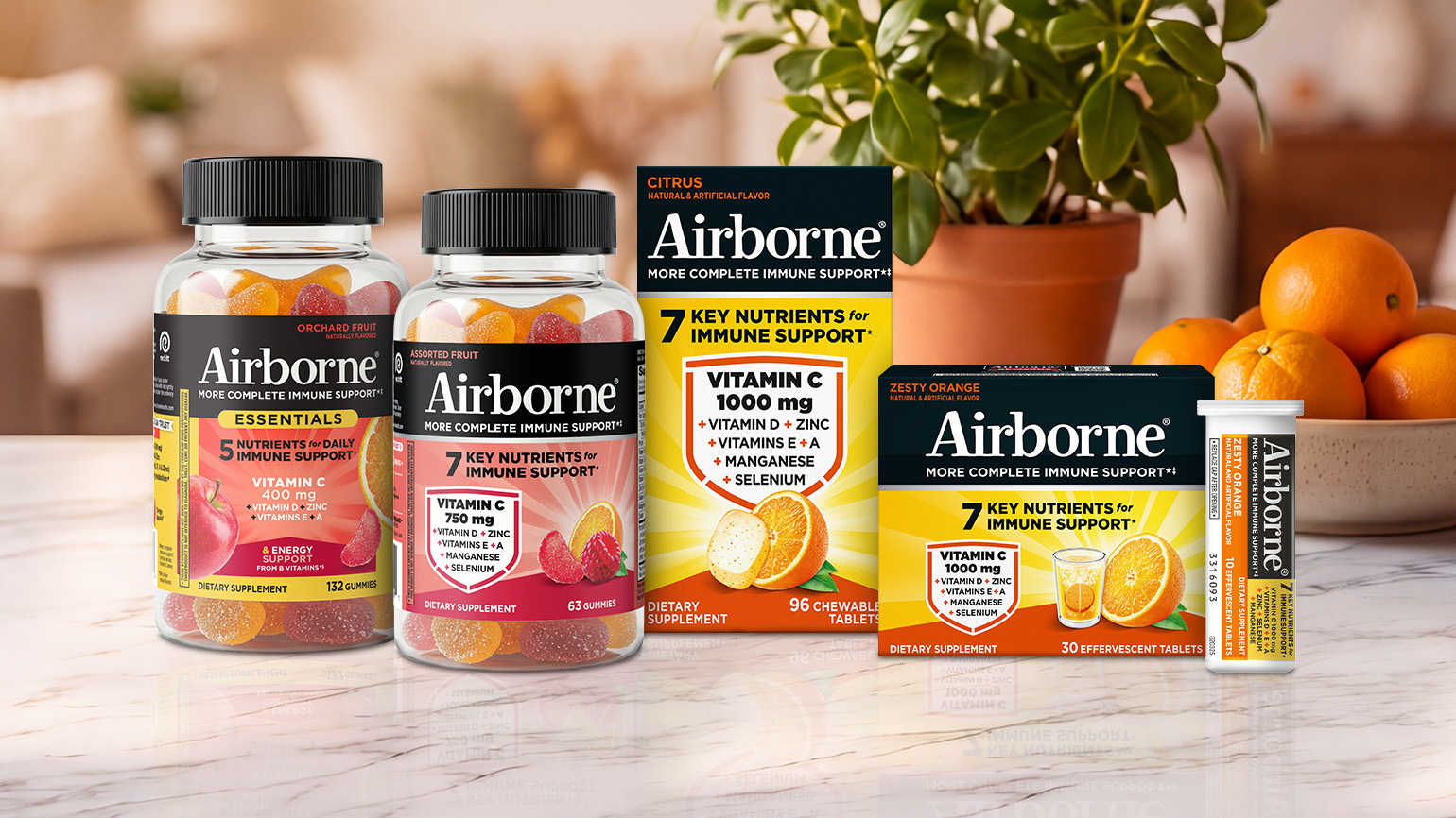 A variety of Airborne immune support supplements displayed on a kitchen counter with a plant and bowl of oranges in the background.