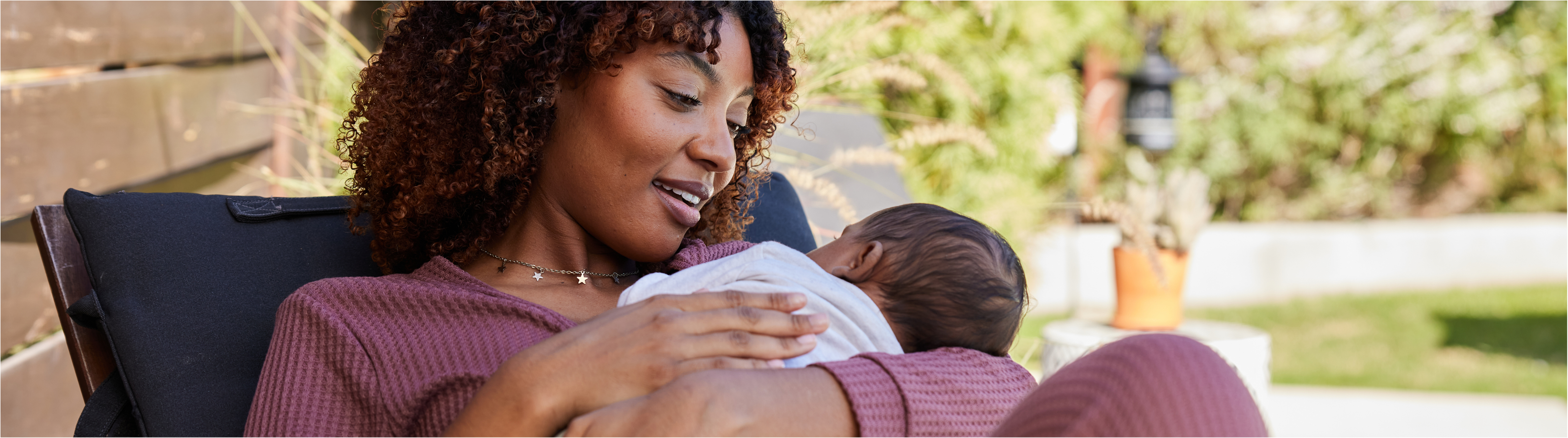 Woman holding a newborn baby while relaxing outdoors in a garden setting