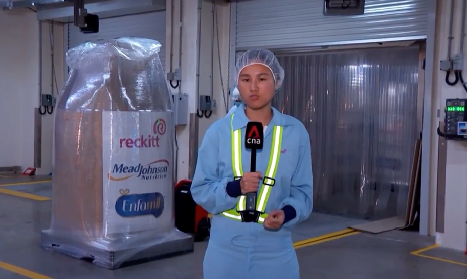Reporter standing inside a Reckitt manufacturing facility during a news segment about infant formula production
