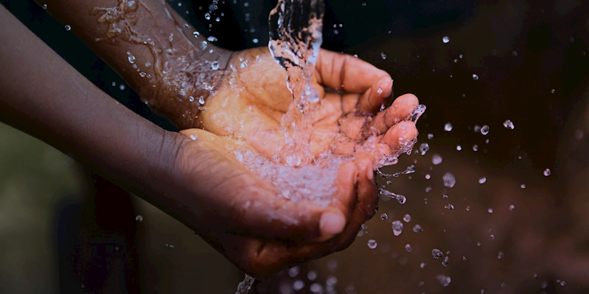 Hands cupping and catching flowing water with splashes visible against a blurred background
